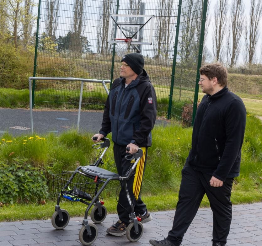 Patient går med rollator sammen med medarbejder på Center for Neurorehabilitering, 2025