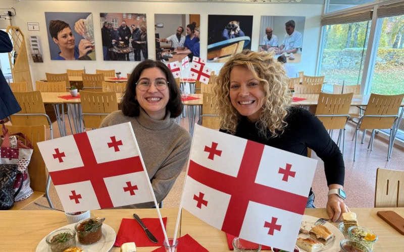 Foto af to kollegaer ved georgisk frokostbord i Filadelfias kantine pyntet med flag fra Georgien.