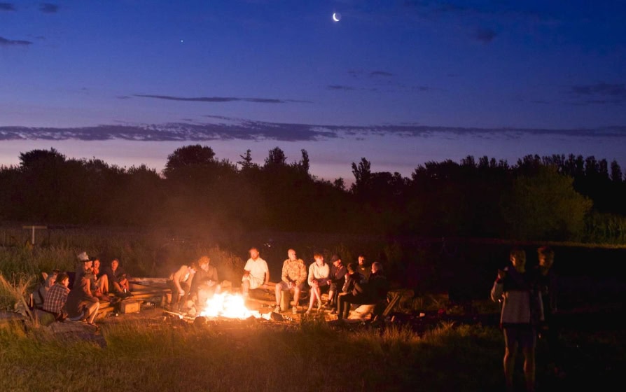 Foto af unge mennesker ved et bål en sommeraften.