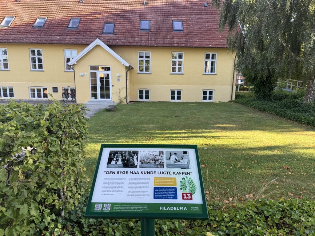Skilt med Filadelfias historie foran det første hus, som Dr. Sell byggede